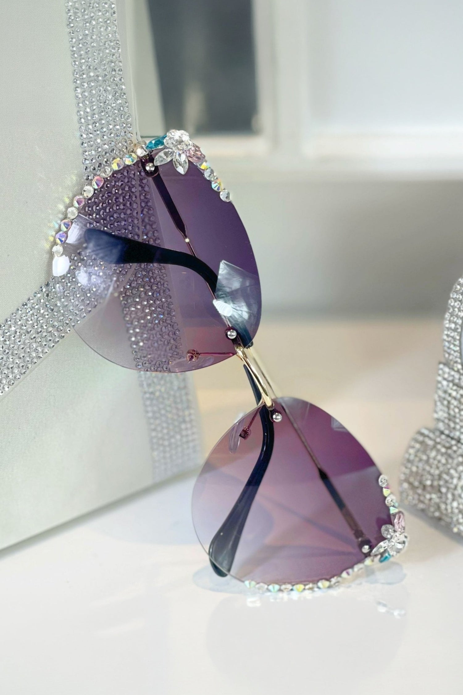 Sunglasses with purple lenses and rhinestone embellishments on a white surface.