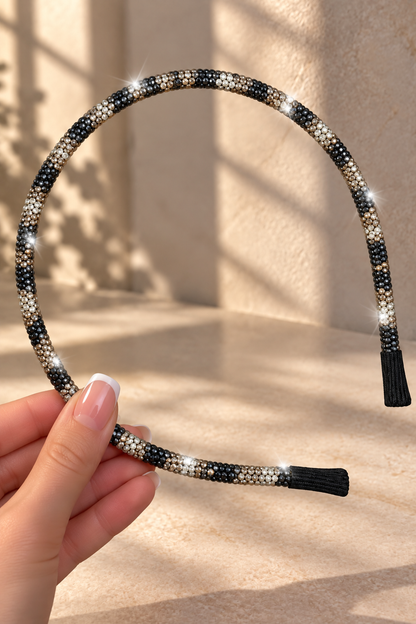 A close-up of a hand holding a leopard print rhinestone-embellished headband against a warm beige wall with soft shadow patterns.