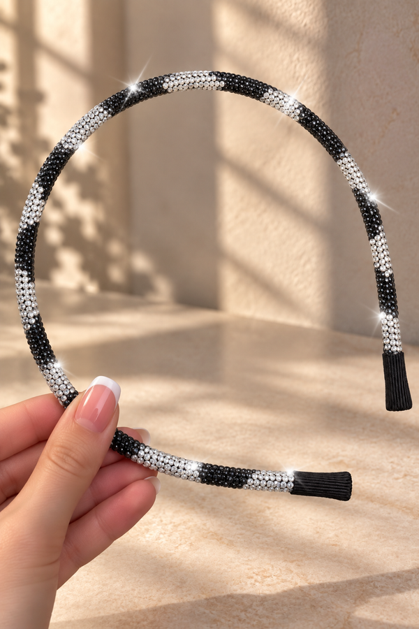 A black and white beaded headband held by a hand, set against a warm beige background with soft shadows.