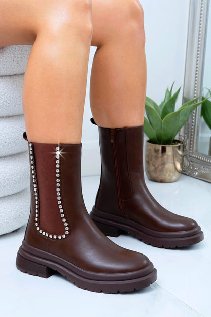 Brown rain boots with decorative elements worn by a person on a light background