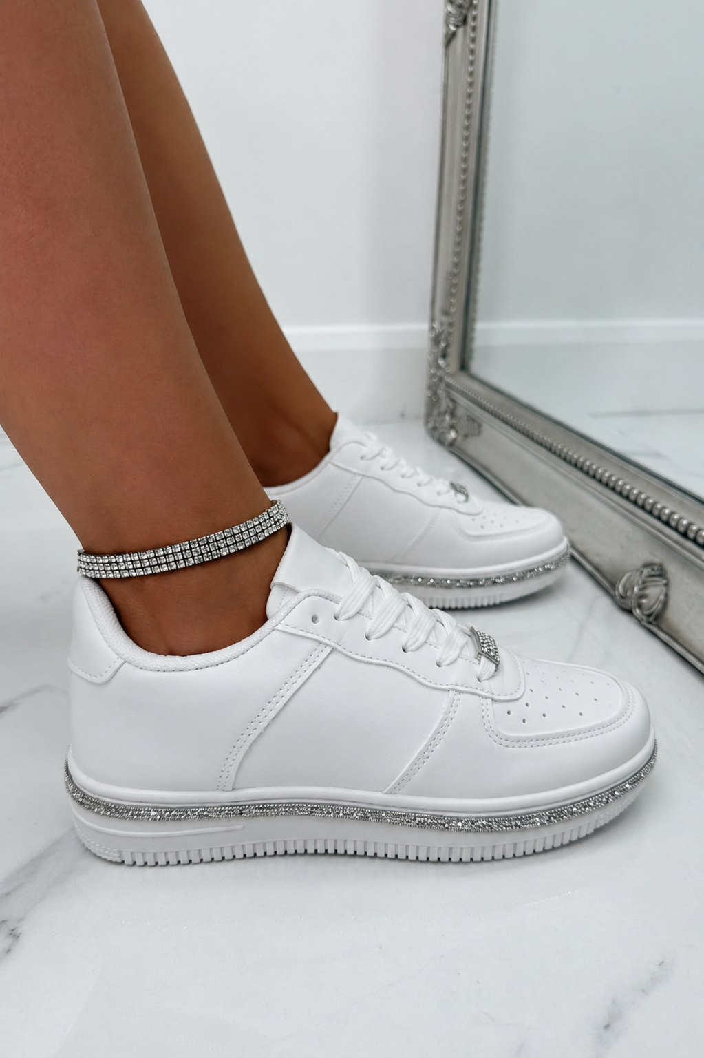 White low-top sneakers with silver rhinestone trim on the soles and laces, shown on a model&