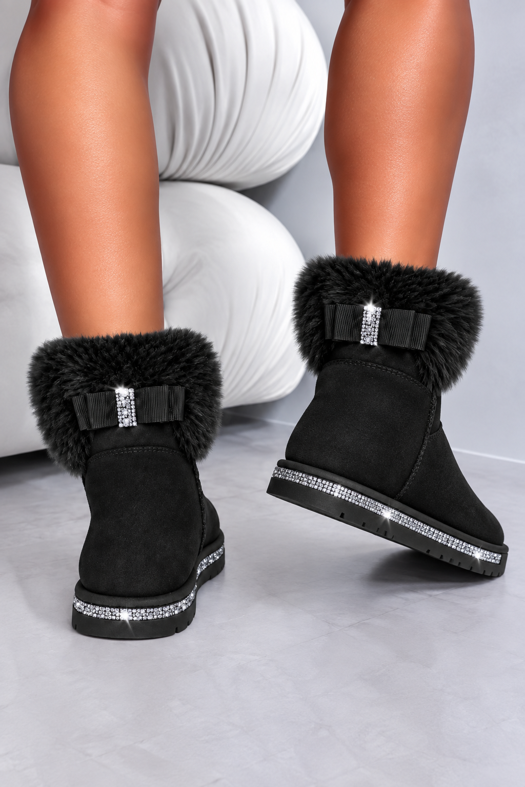 Black faux-suede ankle boots with fluffy black faux-fur trim, black bows, and rhinestone embellishments, shown on a model&