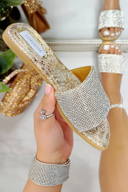 Gold glittery sandal held by a hand with a blurred background