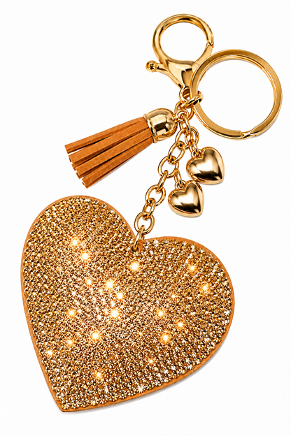 A gold heart-shaped keychain charm covered in sparkling rhinestones, featuring a gold-tone clasp, split key ring, two small heart charms, and a brown faux-leather tassel, shown on a plain white background.