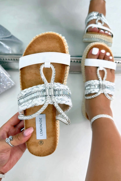 White sandals being held in front of a mirror and worn on one foot