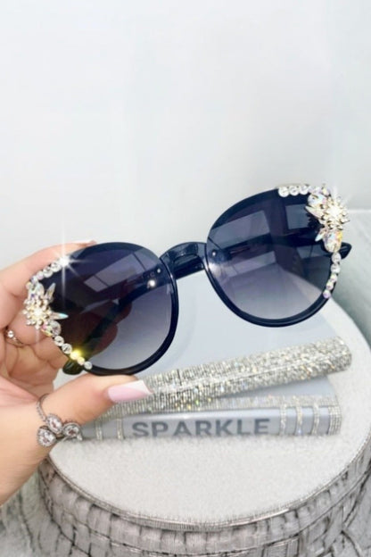 Sunglasses with decorative embellishments held by a hand on a white surface.