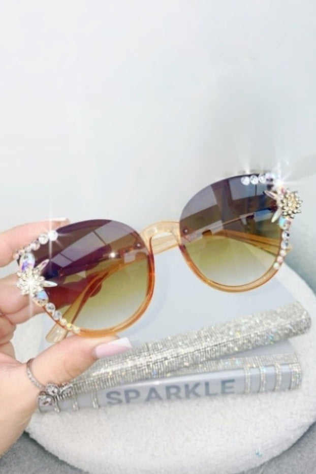 Sunglasses with decorative elements held by a hand on a light gray background