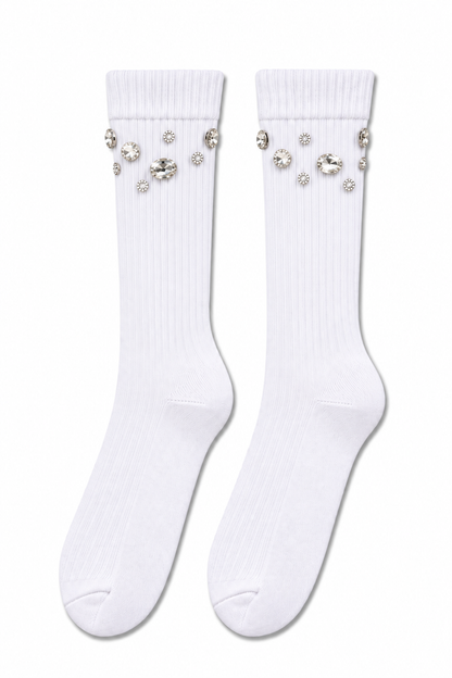 A pair of white ribbed crew socks decorated with clear rhinestone embellishments near the ribbed cuffs, displayed against a solid white background.