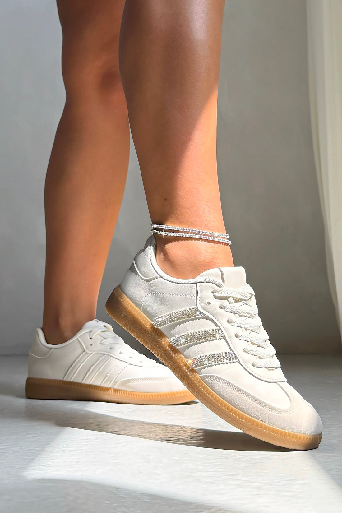 White sneakers with nude embellishments worn by a person on a neutral background