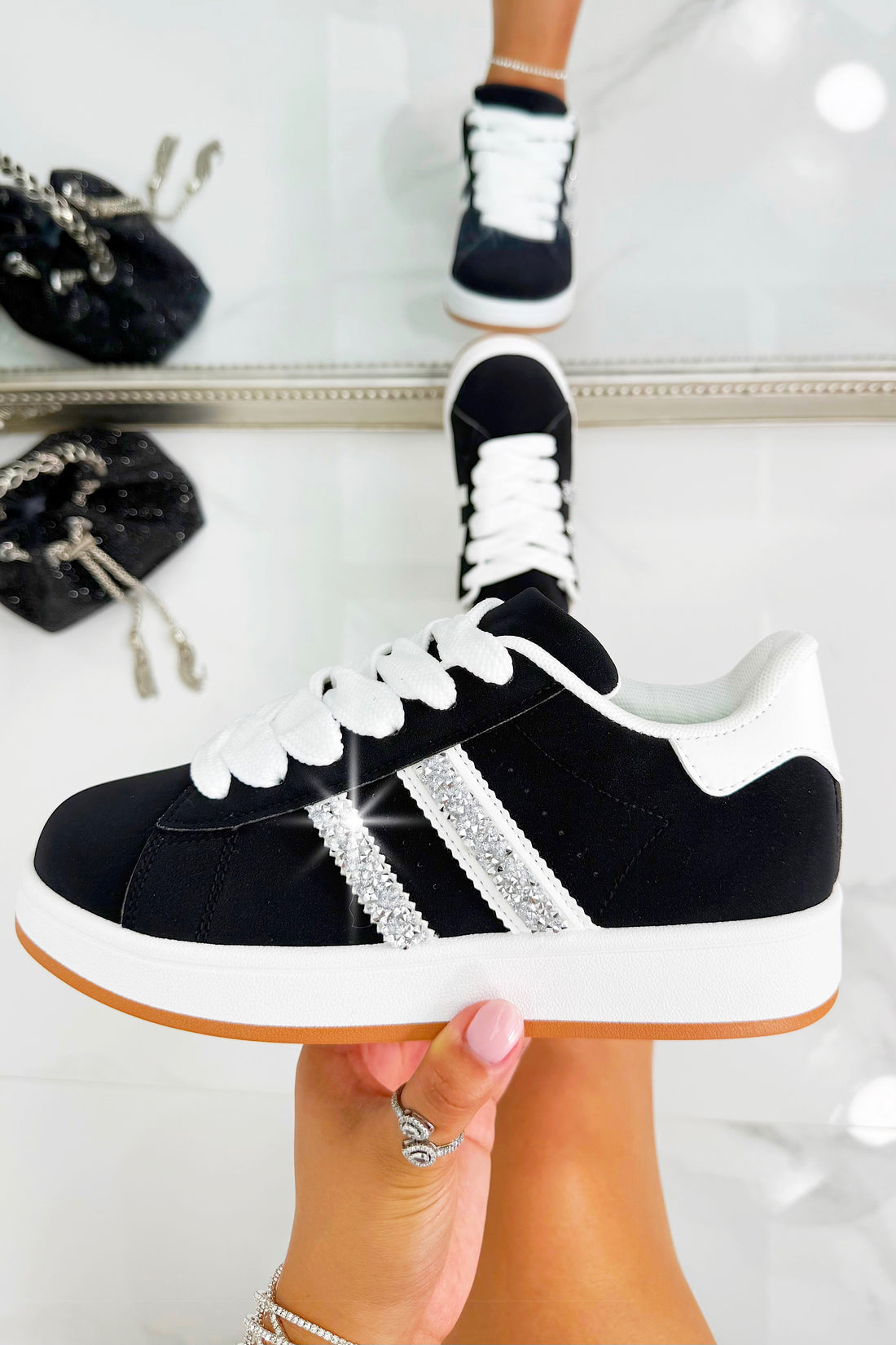 Black and white sneakers with rhinestone details held by a hand against a white background