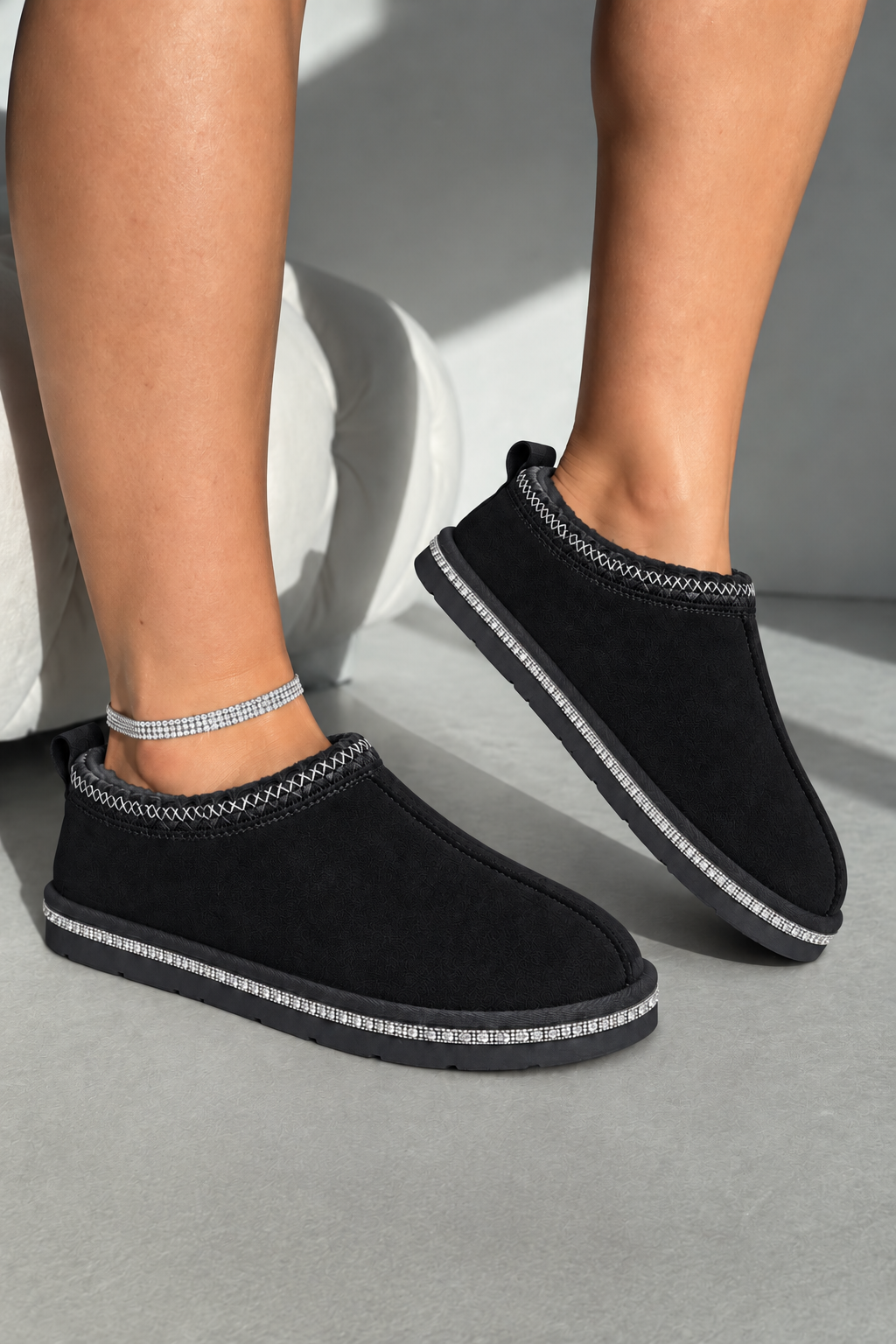 A pair of black slip-on slippers with silver rhinestone trim, shown on a model&