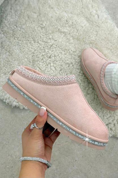 Pink slip-on shoes with rhinestone trim held by a hand on a light background