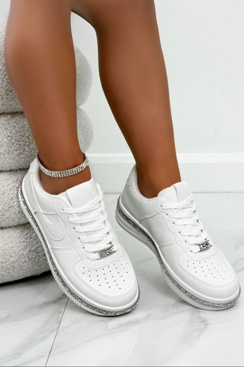 White sneakers with silver accents worn by a person sitting on an ottoman