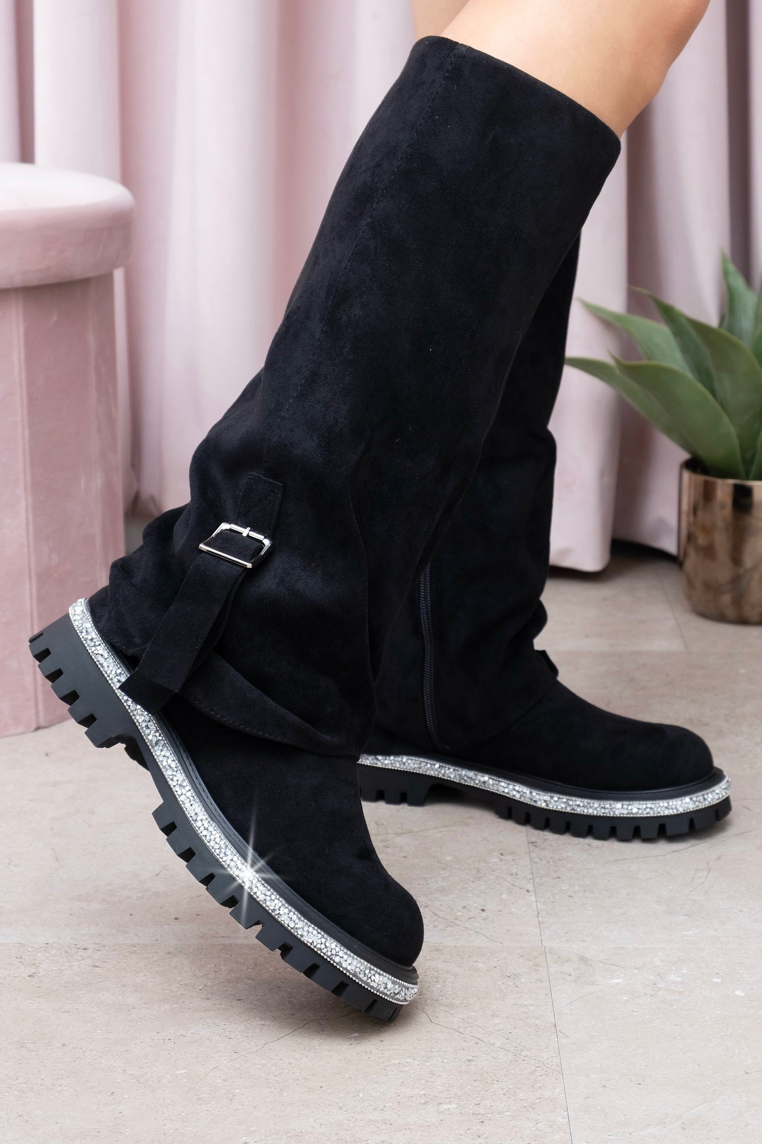 Black knee-high boots with silver accents worn by a person indoors.
