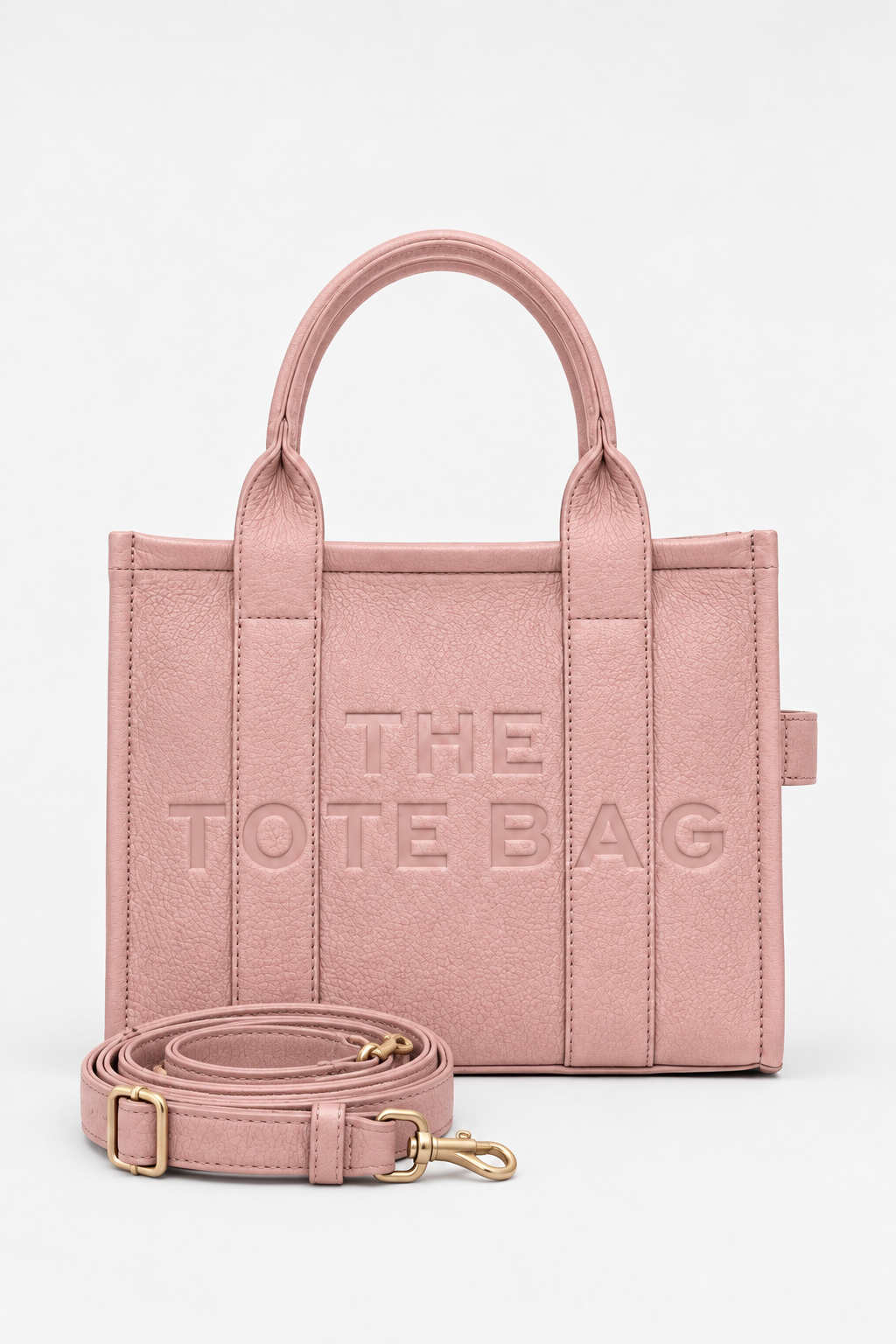 Dusty Rose faux leather structured tote bag with two rounded top handles, embossed. "THE TOTE BAG" lettering on the front, vertical stitched panels, contrast edging and gold- tone stud details. 