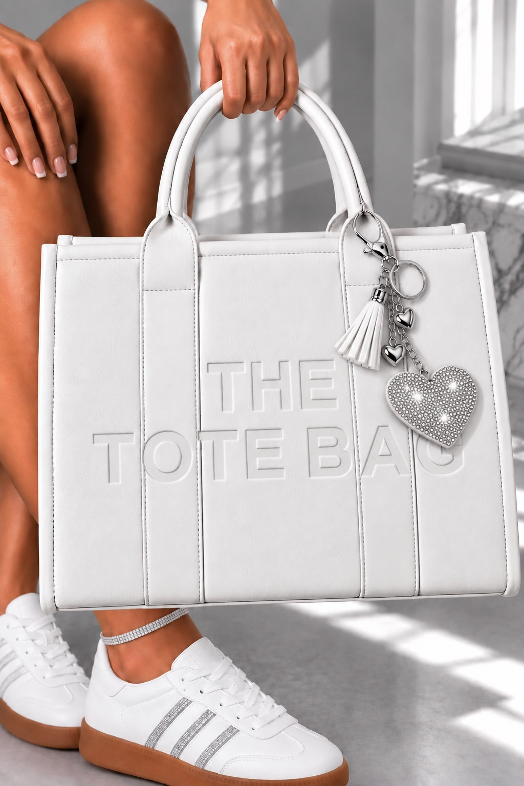 A white faux-leather tote bag with embossed vertical panels and the text &