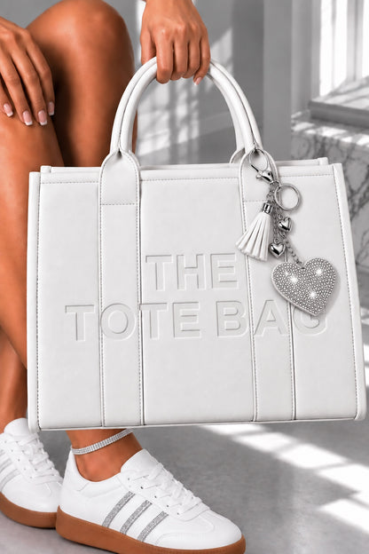 A white faux-leather tote bag with embossed vertical panels and the text &