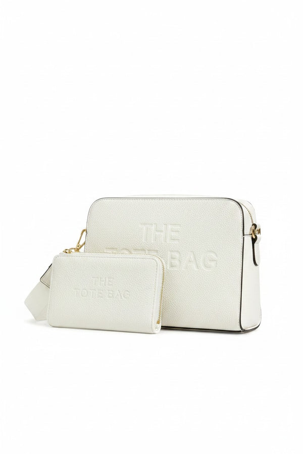 White faux leather cross body bag with a rectangular shape, rounded corners, embossed, "THE TOTE BAG" lettering on the front, gold-tone clips and a wide adjustable matching shoulder strap with a gold tone buckle. With a matching zip up purse.