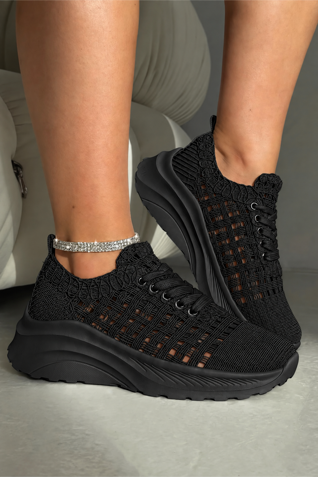 A pair of black knit lace-up sneakers with chunky black platform soles, shown on a model&