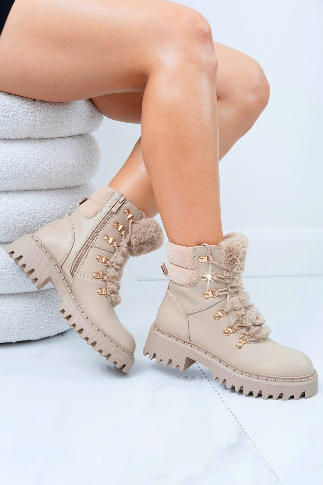 Beige winter boots with fur lining worn by a person sitting on a white surface.