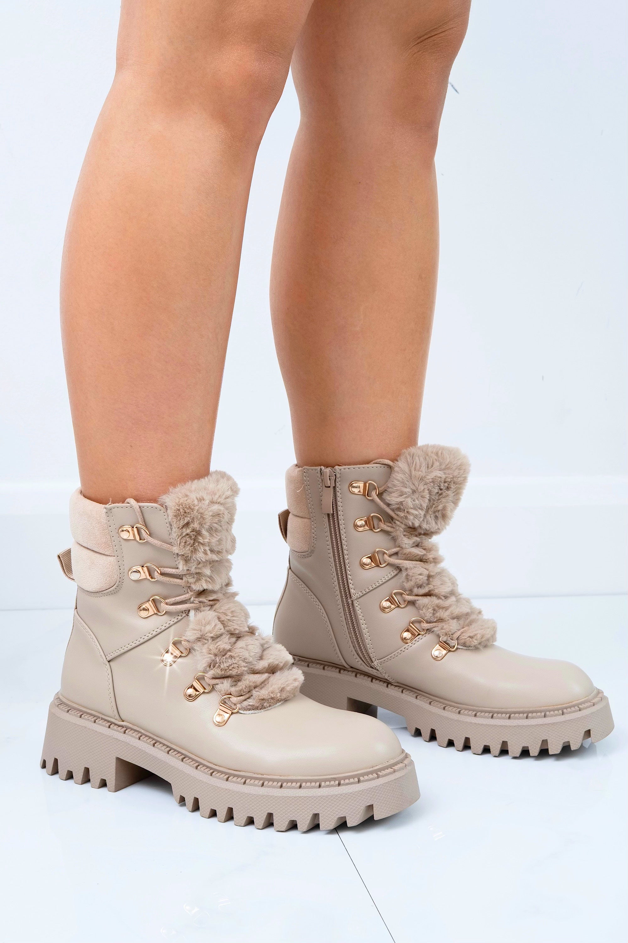 Beige winter boots with fur trim worn by a person on a light gray background