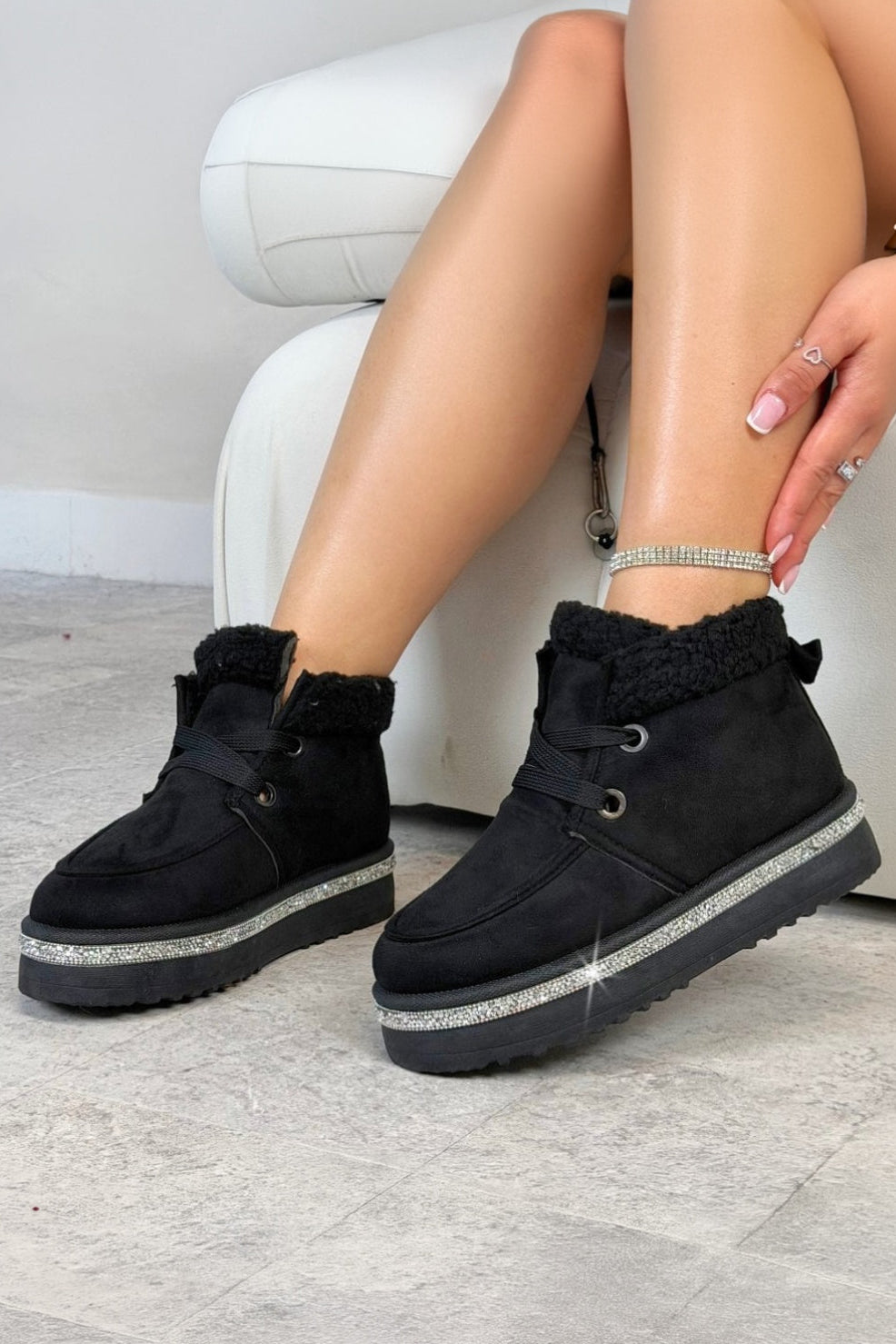 Black winter boots with glittery sole worn by a person sitting on a white chair.