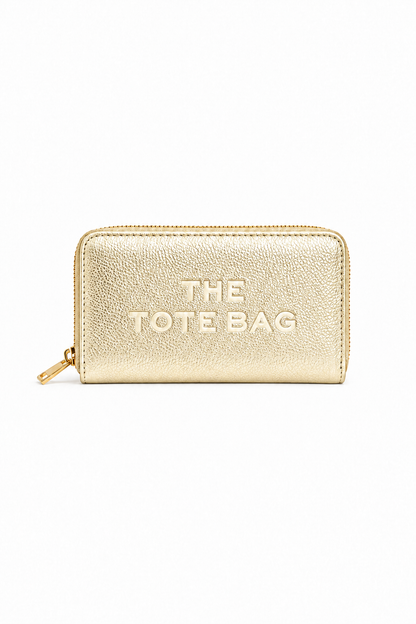 Metallic Gold rectangular zip-around purse with embossed "THE TOTE BAG" lettering on the front, contrast stitching around the edges and a gold-tone zip fastening with a matching pull tab. Set against a plain white background.