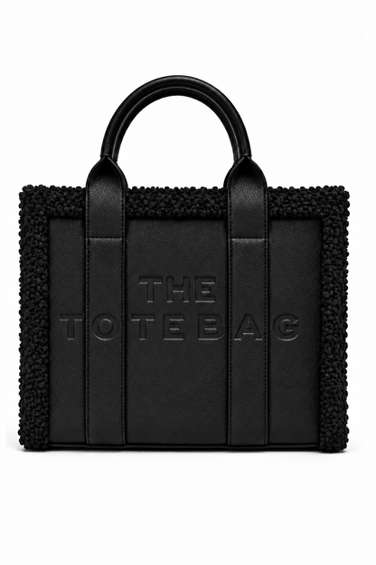 Black tote handbag with structured rectangular shape, rounded top handles, smooth central panels, and a textured black trim along the top and sides. Features embossed, "THE TOTE BAG" lettering on the front and contrasting vertical handle straps. 