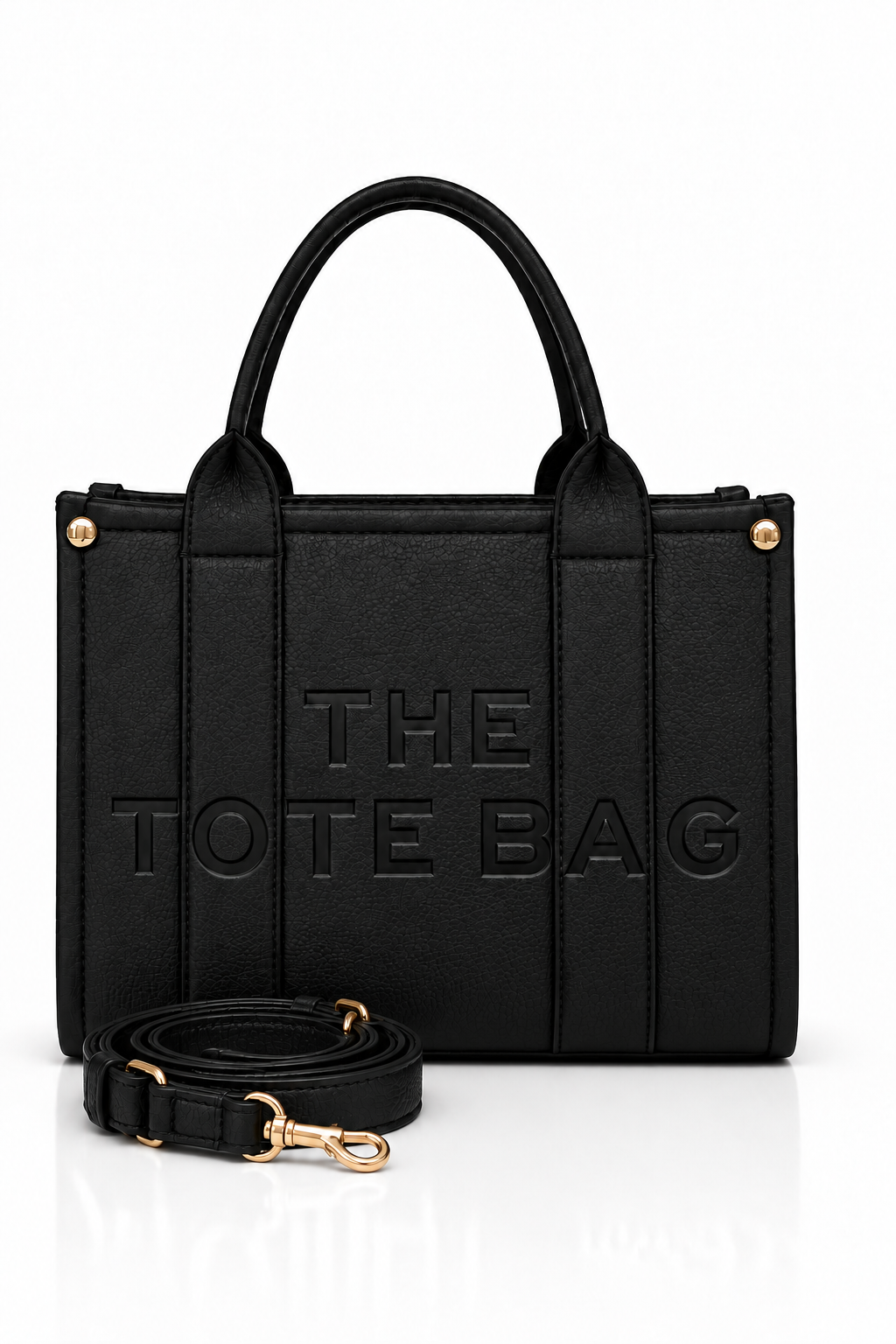 Black faux leather tote bag with two rounded top handles, embossed "THE TOTE BAG" lettering on the front, contrast stitching, gold tone hardware and a detachable adjustable black shoulder strap.