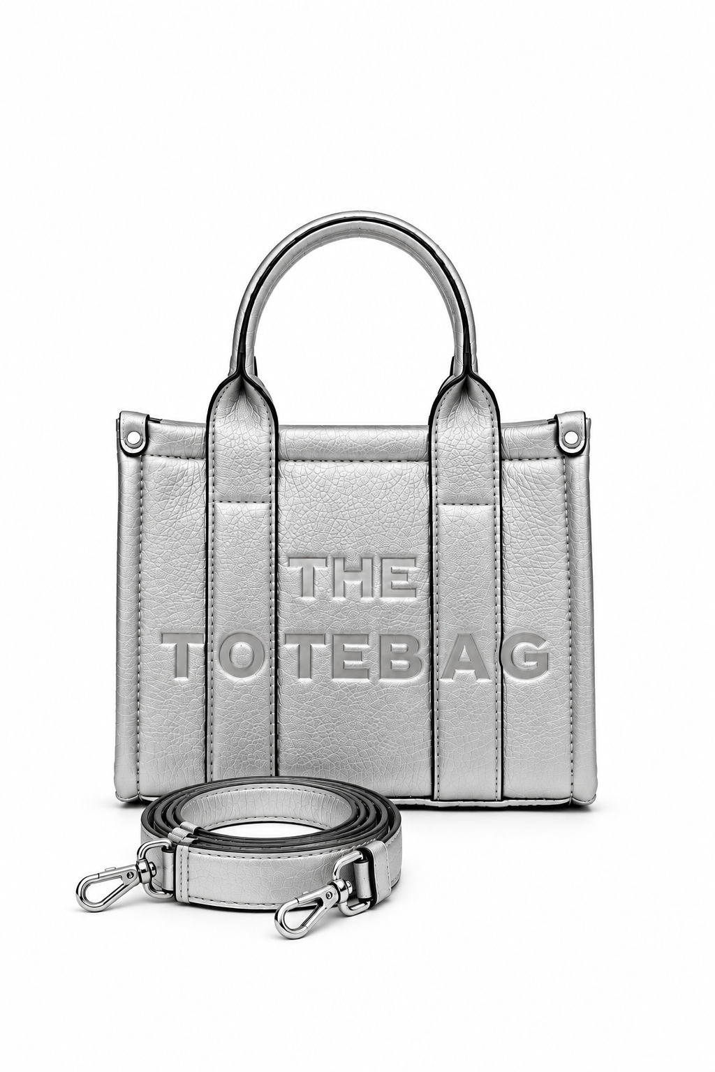 Beige mini faux leather structured tote bag with two rounded top handles, vertical stitched panels, matching tonal stitching and subtle embossed "THE TOTE BAG" lettering on the front. Silver shoulder strap pictured in front of bag. 