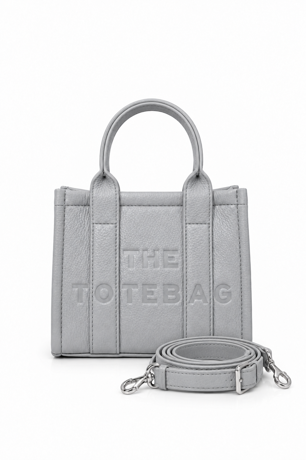 Grey structured faux leather mini tote bag with two rounded top handles, embossed. "THE TOTE BAG" lettering on the front, vertical stitched panels, contrast edging.  With grey-tone strap pictured in front of the bag.