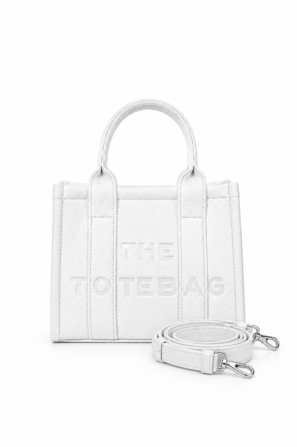 White faux leather mini Tote bag with with two rounded top handles, embosses "THE TOTE BAG" lettering on the front, vertical stitched panels and a small side tab detail. with a detachable matching shoulder strap. 