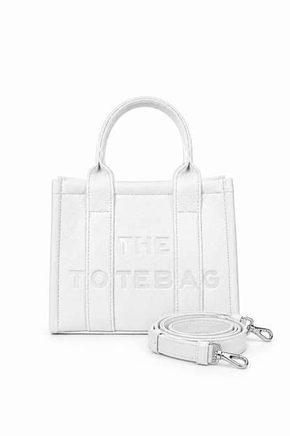 White faux leather mini Tote bag with with two rounded top handles, embosses "THE TOTE BAG" lettering on the front, vertical stitched panels and a small side tab detail. with a detachable matching shoulder strap. 