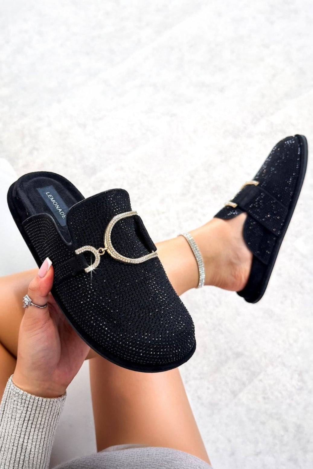 Black slip-on shoes with a decorative buckle held by a person on a light gray background