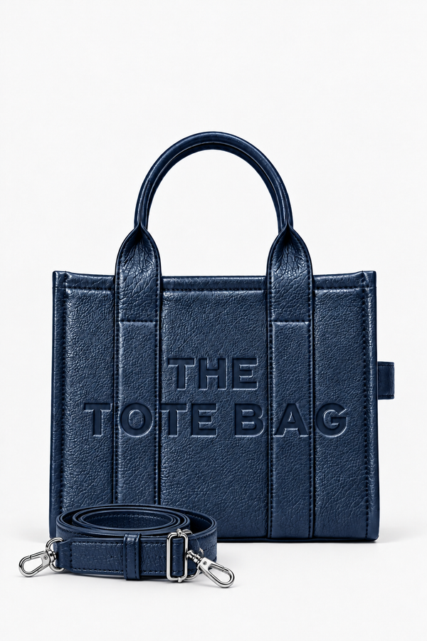 Blue faux leather structured tote bag with two rounded top handles, embossed. "THE TOTE BAG" lettering on the front, vertical stitched panels, contrast edging. With blue-tone strap pictured in front of the bag.