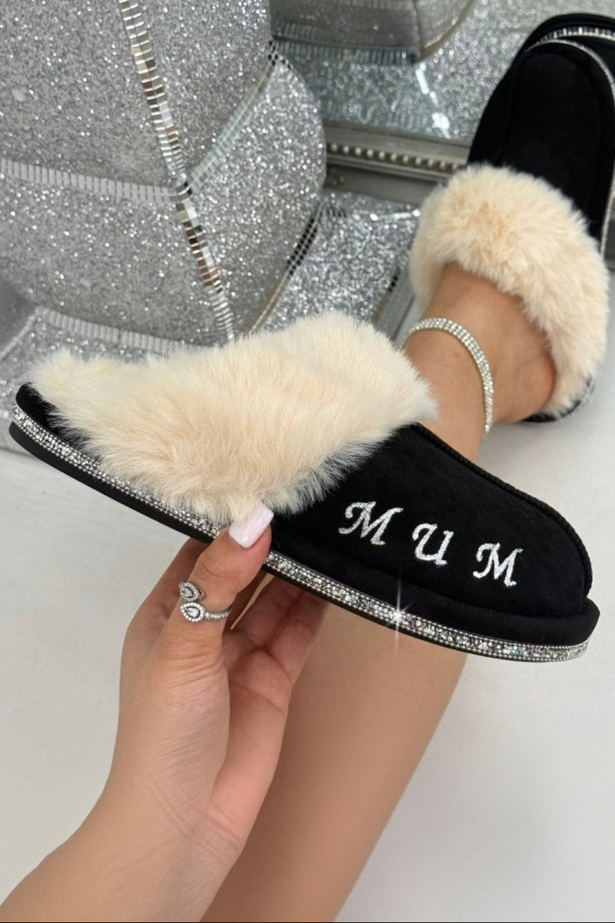 Black slippers with white fur trim held by a hand in front of a sparkly background