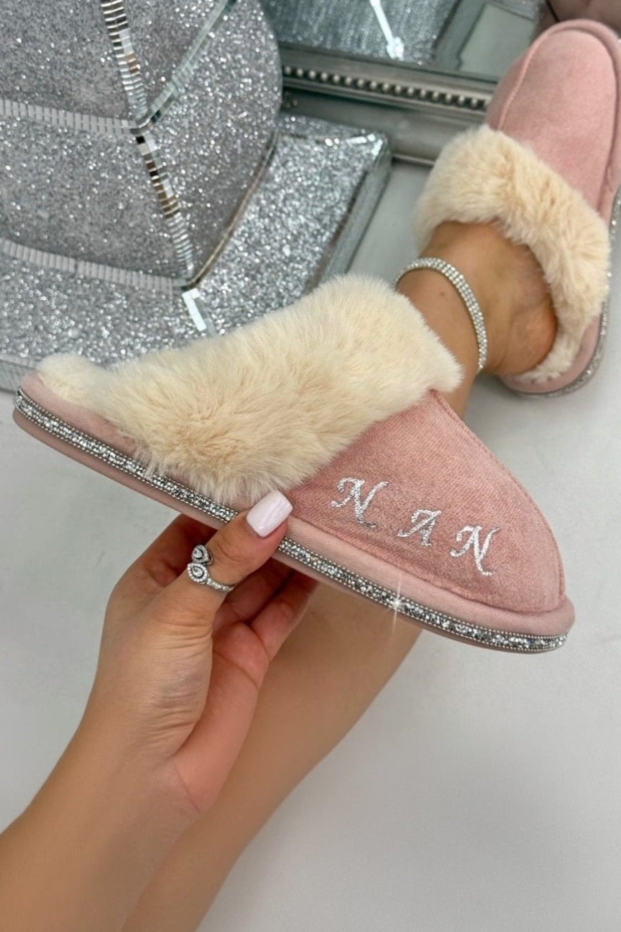 Pink slippers with fur trim held by a hand in front of a mirror.