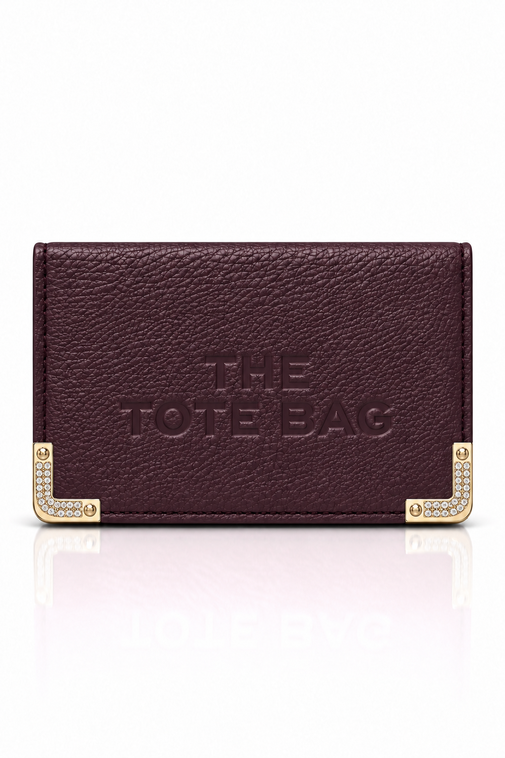 Plum textured tote purse with embossed "The Tote Bag" lettering on the front and cream and gold-tone decorative metal corner protectors with stud detailing. Set against a plain white background.