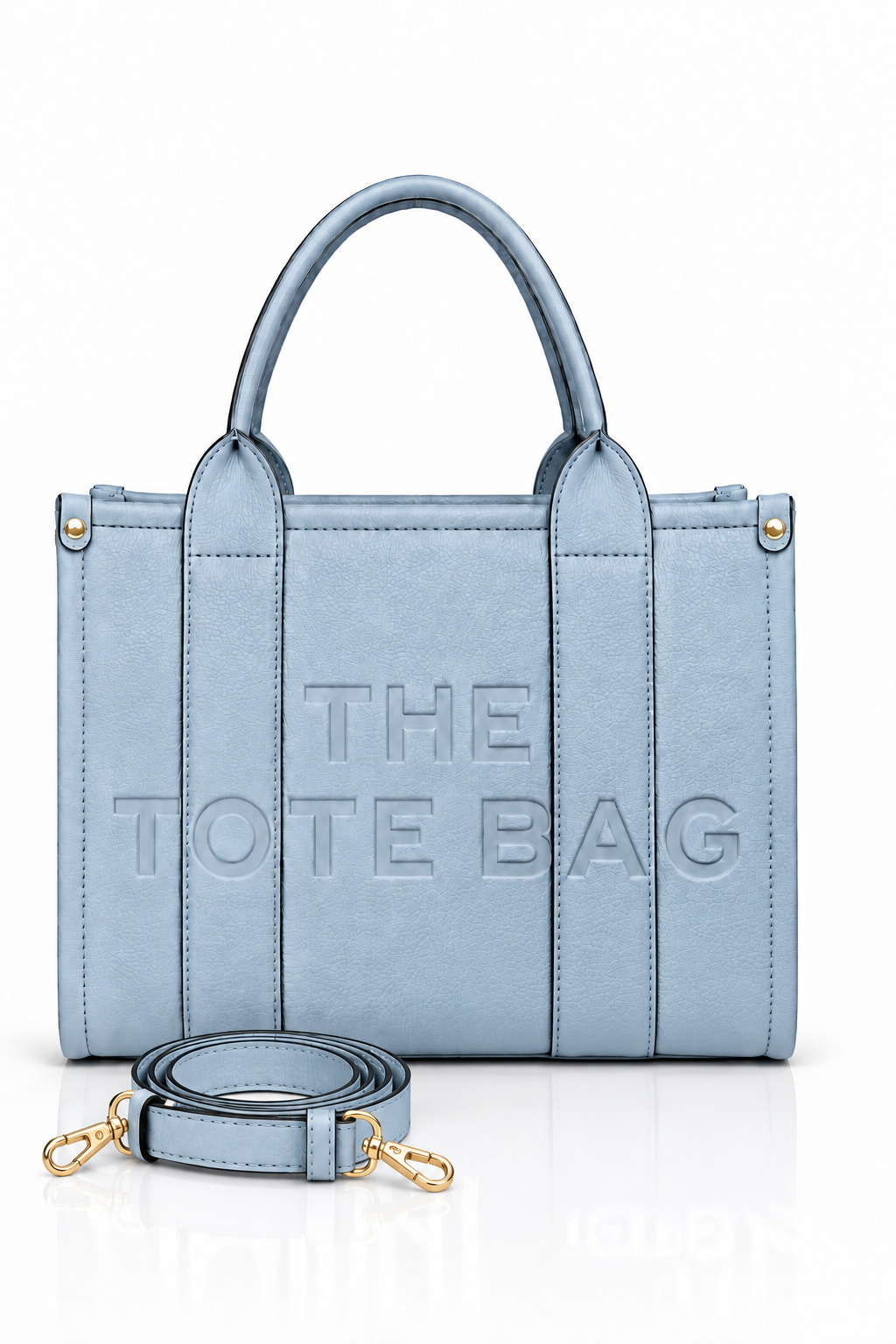 Blue faux leather tote bag with two rounded top handles, embossed "THE TOTE BAG" lettering on the front, contrast stitching and a detachable adjustable blue shoulder strap.
