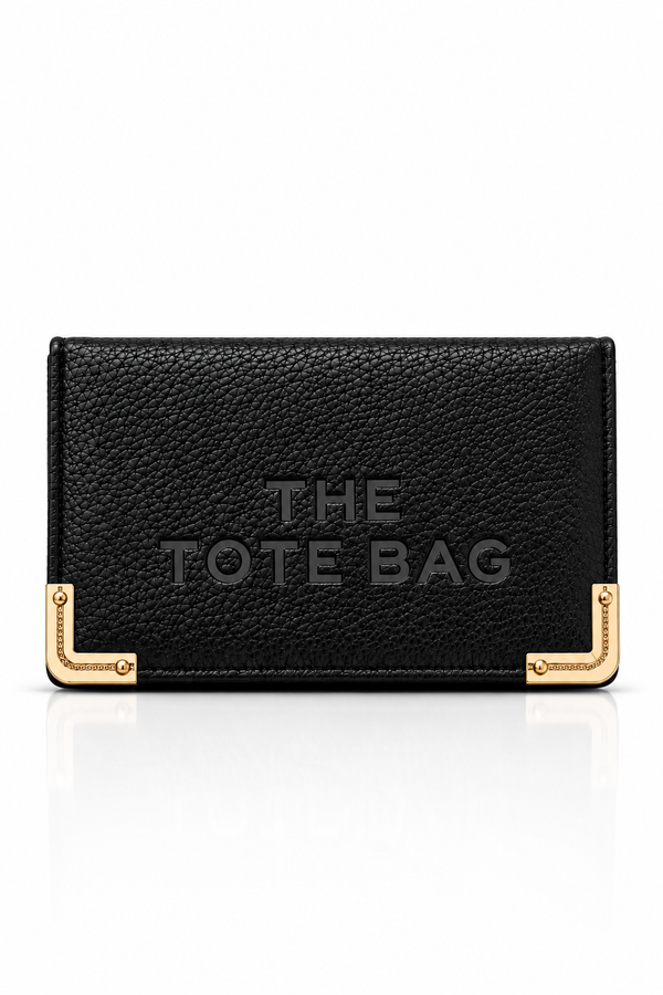 Black textured faux leather purse featuring THE TOTE BAG lettering on the front, with contrasting gold tone metal corner protectors and decorative detailing. Set against a plain white background.