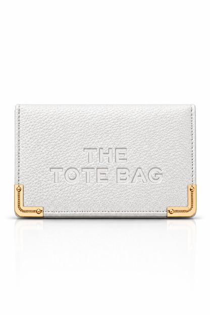 White textured tote purse with embossed "The Tote Bag" lettering on the front, featuring gold tone metal corner protectors with decorative stud detailing. 