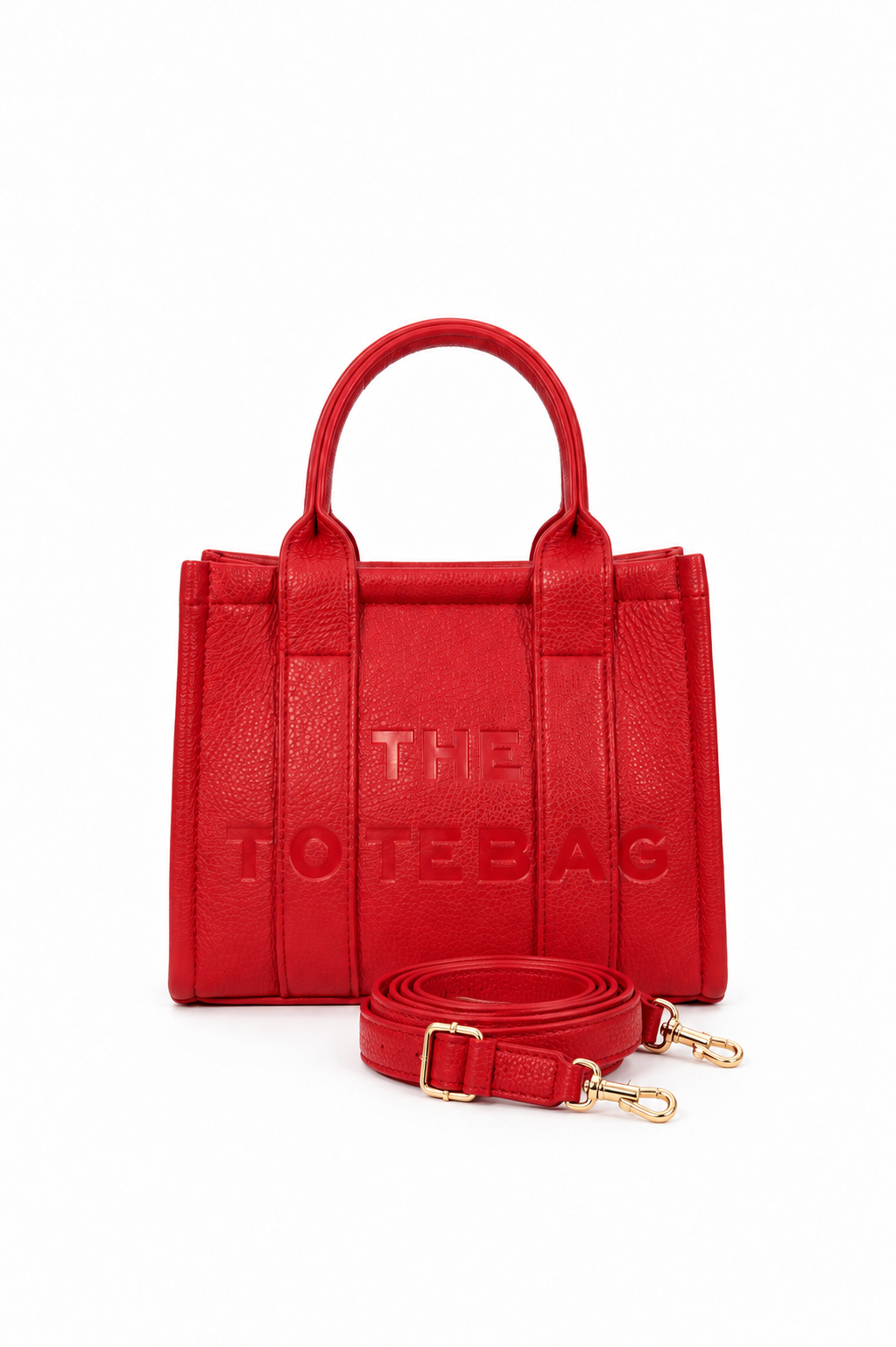 Red structured faux leather mini tote bag with two rounded top handles, embossed. "THE TOTE BAG" lettering on the front, vertical stitched panels, contrast edging.  With red-tone strap pictured in front of the bag.