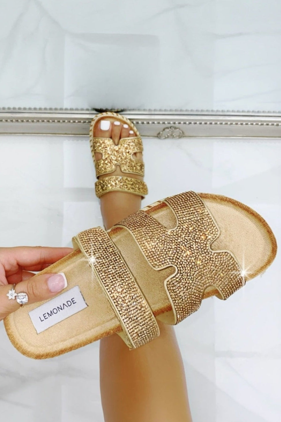 Rose gold embellished sandals being worn on a white background
