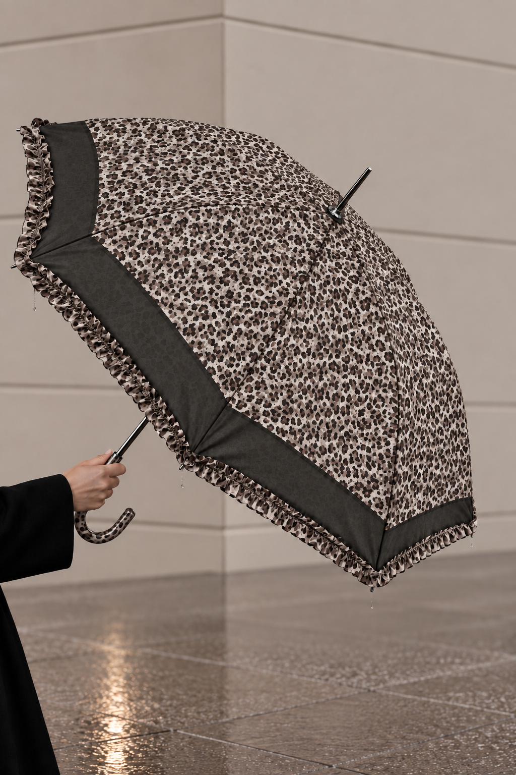 A person holds an open leopard-print umbrella with a dark gray ruffled trim and a curved black handle in a modern indoor setting with tiled floors.