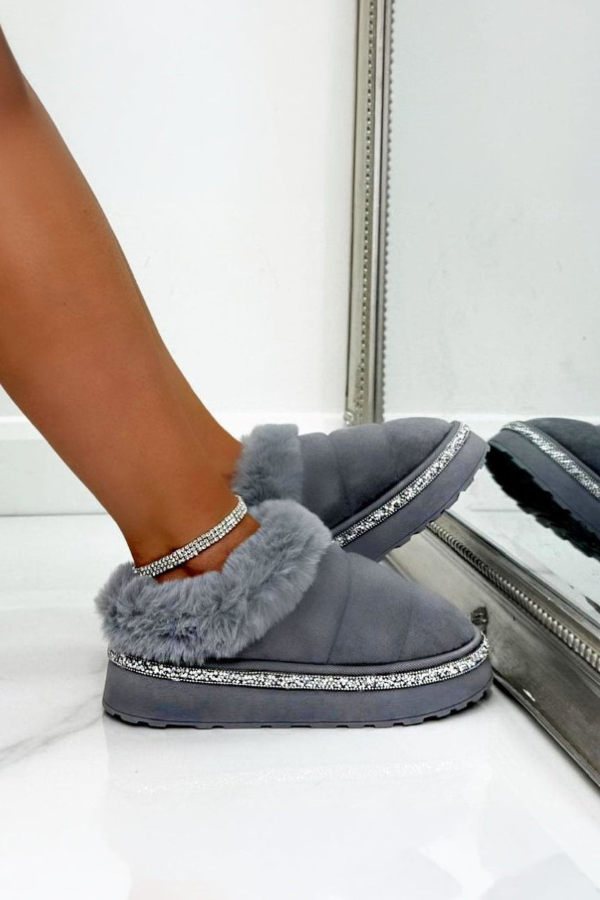Gray slippers with fluffy trim worn by a person, reflected in a mirror.