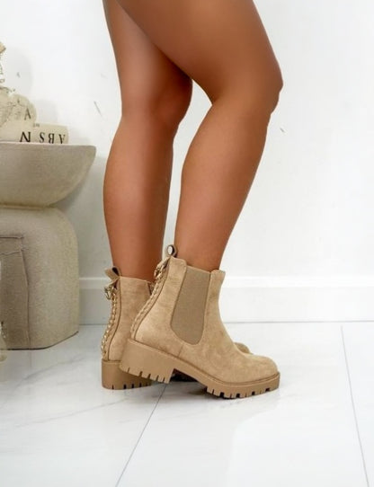 Beige boots worn by a person on a white floor with a neutral-colored rug.