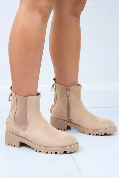 Beige Chelsea boots worn by a person on a light gray background