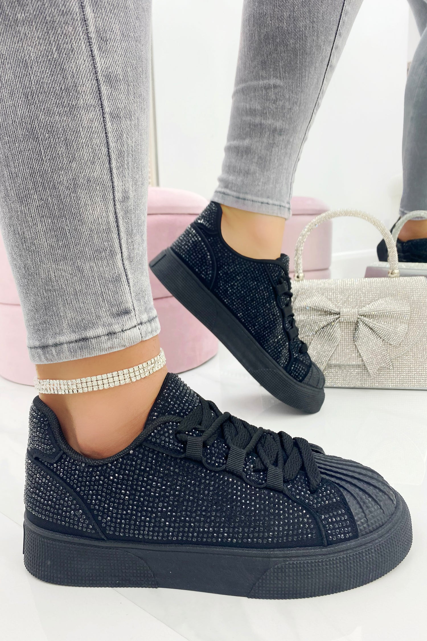 Black embellished sneakers worn with gray jeans on a white background