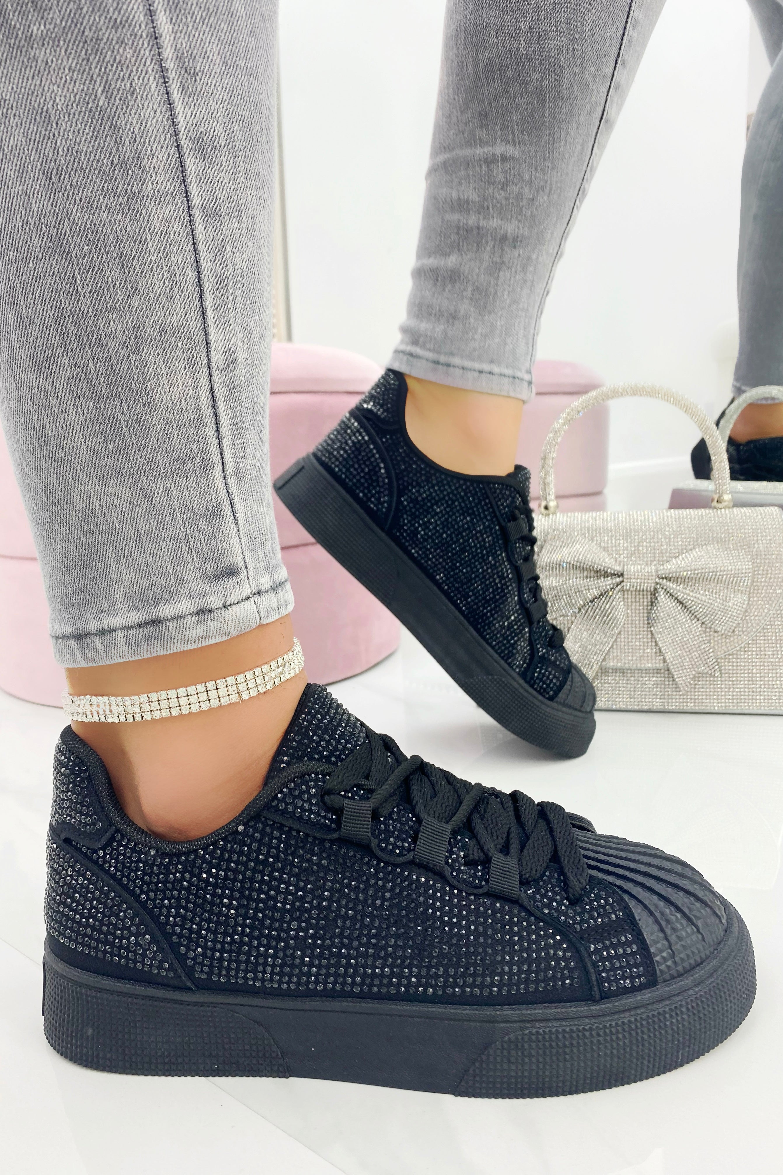 Black embellished sneakers worn with gray jeans on a white background