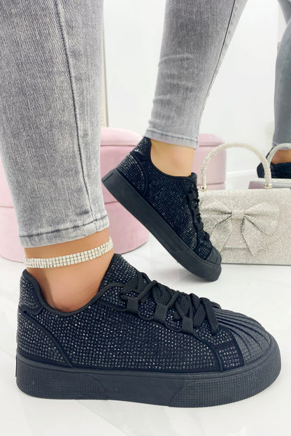 Black embellished sneakers worn with gray jeans on a white background